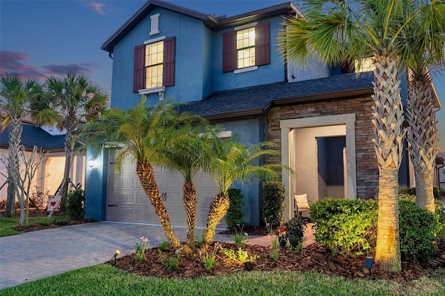 traditional home featuring stucco siding, stone siding, driveway, and a shingled roof