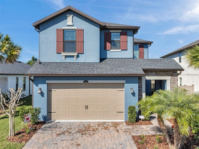 traditional home featuring stucco siding, decorative driveway, a garage, and roof with shingles