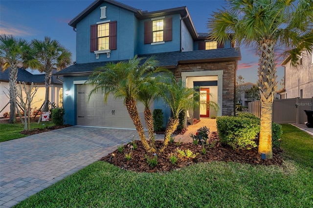 traditional home with stone siding, stucco siding, decorative driveway, and fence