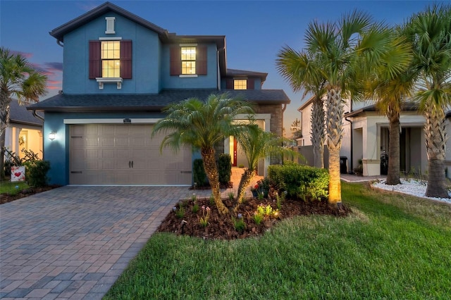 traditional-style home with decorative driveway, a lawn, an attached garage, and stucco siding