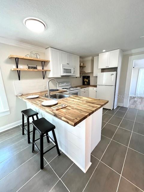 kitchen featuring white appliances, open shelves, butcher block countertops, a sink, and dark tile patterned floors