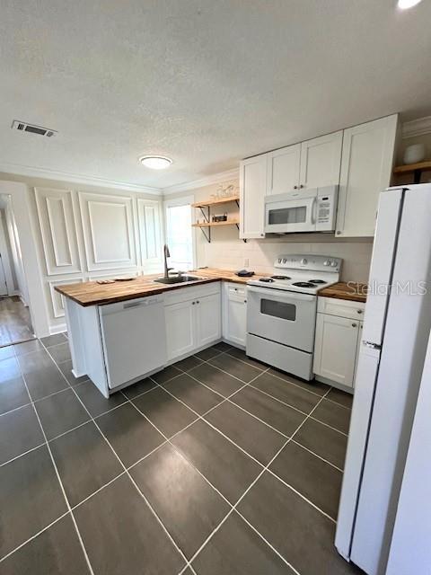 kitchen with a sink, white appliances, dark tile patterned flooring, and wooden counters