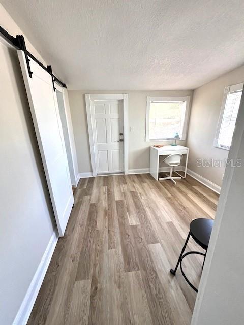 interior space with baseboards, a textured ceiling, a barn door, and wood finished floors