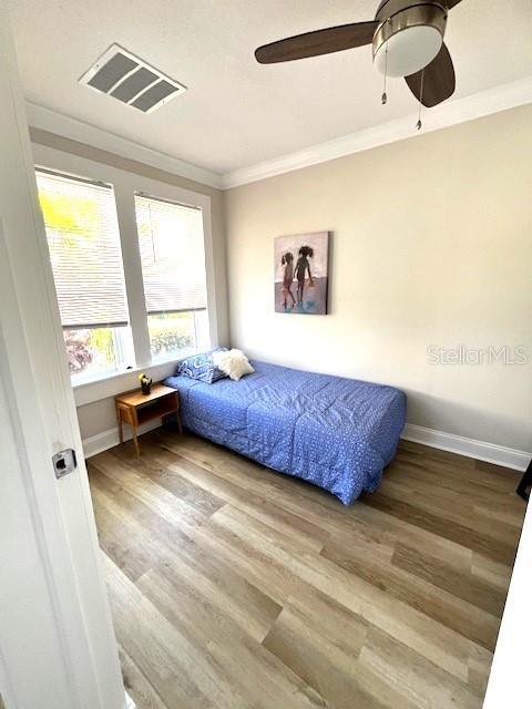 bedroom featuring baseboards, wood finished floors, visible vents, and ornamental molding