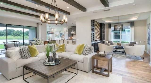 living area featuring light wood-type flooring, beam ceiling, visible vents, a raised ceiling, and a chandelier