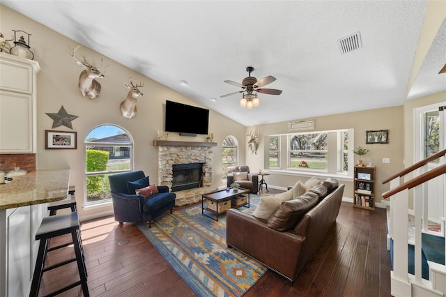 living room featuring visible vents, dark wood finished floors, lofted ceiling, ceiling fan, and a stone fireplace