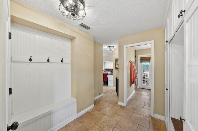 mudroom with a textured ceiling, baseboards, visible vents, and stone tile flooring