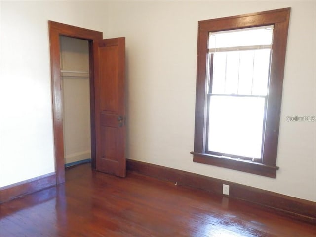 unfurnished bedroom featuring baseboards, multiple windows, and dark wood-style flooring