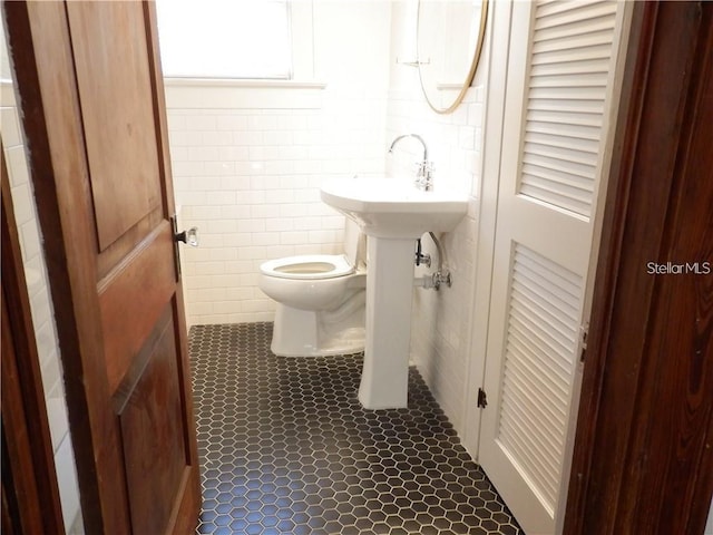 half bath with tile patterned flooring, toilet, and tile walls