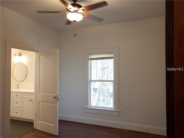 unfurnished bedroom with ensuite bathroom, dark wood-type flooring, and baseboards