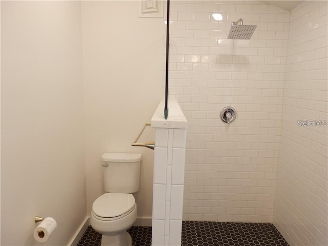 bathroom featuring baseboards, toilet, tile patterned flooring, and a tile shower