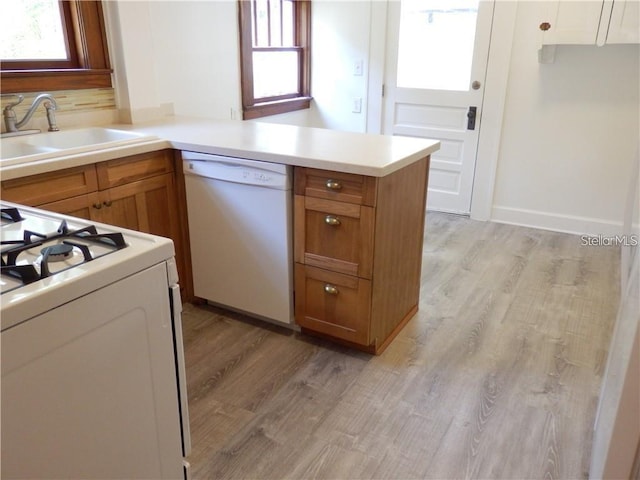 kitchen with white appliances, light wood-type flooring, a peninsula, a sink, and brown cabinets