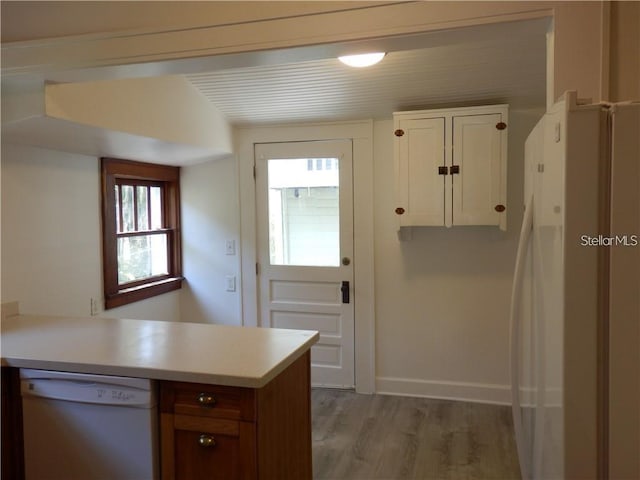 kitchen with baseboards, light countertops, a peninsula, light wood-style floors, and white appliances