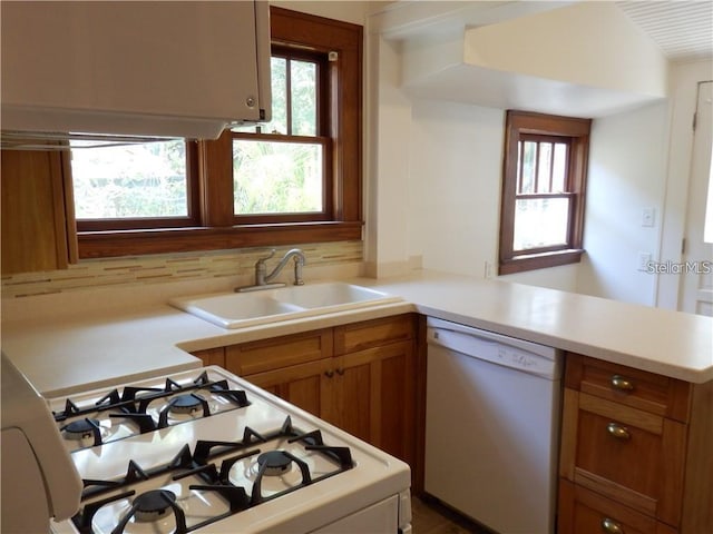 kitchen featuring a sink, white appliances, a peninsula, light countertops, and decorative backsplash