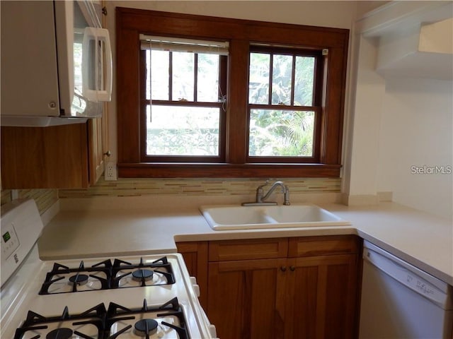 kitchen featuring white appliances, brown cabinetry, a sink, decorative backsplash, and light countertops