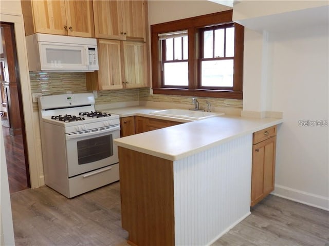 kitchen featuring white appliances, light wood-style floors, a peninsula, and a sink