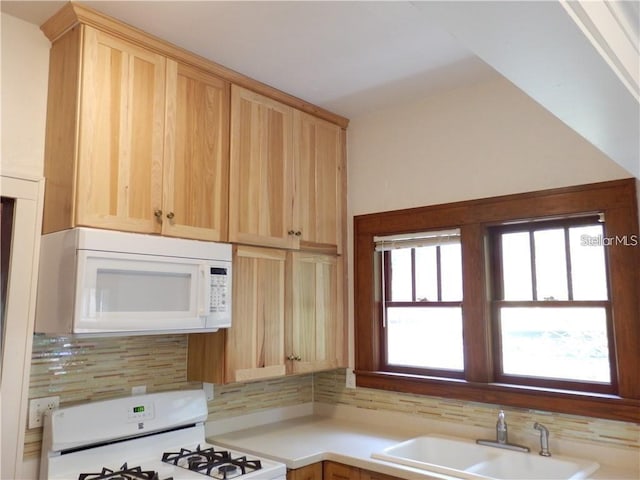 kitchen featuring light brown cabinets, decorative backsplash, white appliances, and a sink