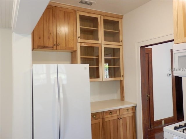 kitchen with visible vents, white appliances, glass insert cabinets, and light countertops