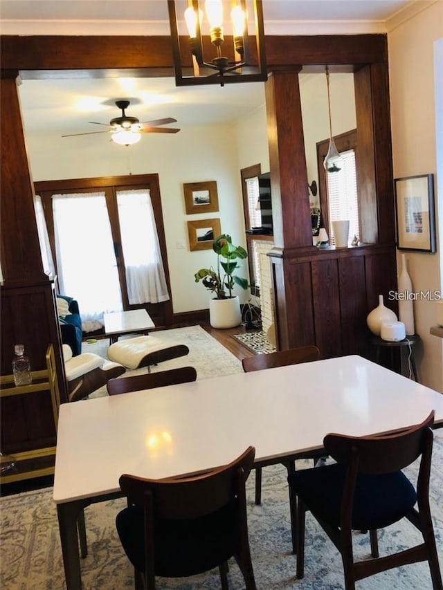 dining area featuring ceiling fan with notable chandelier, baseboards, ornate columns, and wood finished floors