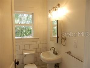 half bath with a sink, toilet, and tile walls