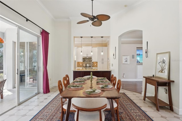 dining space with arched walkways, ceiling fan, crown molding, and baseboards