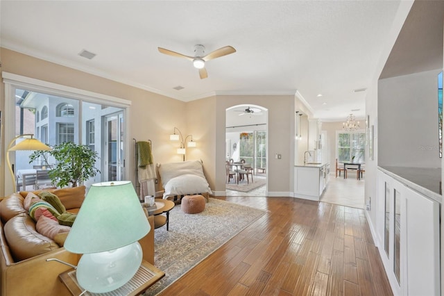 living room with baseboards, visible vents, crown molding, ceiling fan with notable chandelier, and light wood-type flooring