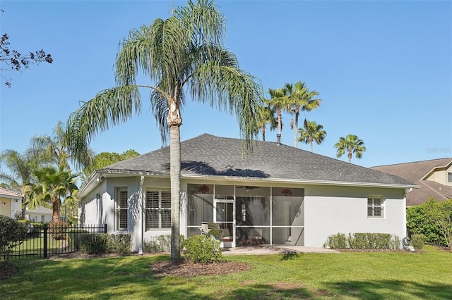 rear view of property featuring fence, roof with shingles, a yard, a sunroom, and stucco siding