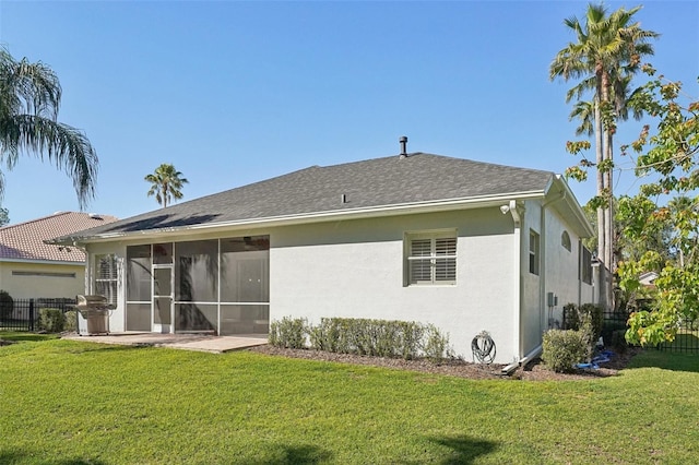 rear view of house featuring stucco siding, fence, a lawn, and a sunroom