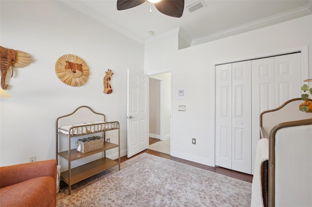 bedroom with wood finished floors, baseboards, visible vents, ornamental molding, and a closet