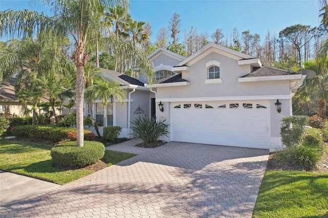 view of front of property featuring decorative driveway, an attached garage, and stucco siding