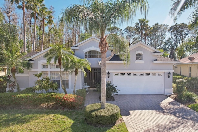 mediterranean / spanish-style home with decorative driveway, an attached garage, and stucco siding