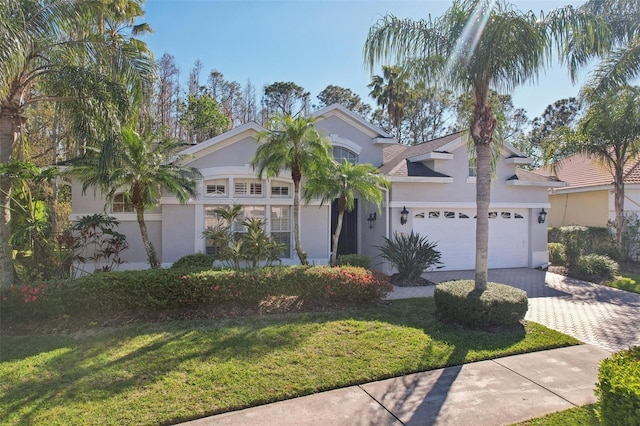 view of front of property with stucco siding, a front yard, decorative driveway, and a garage