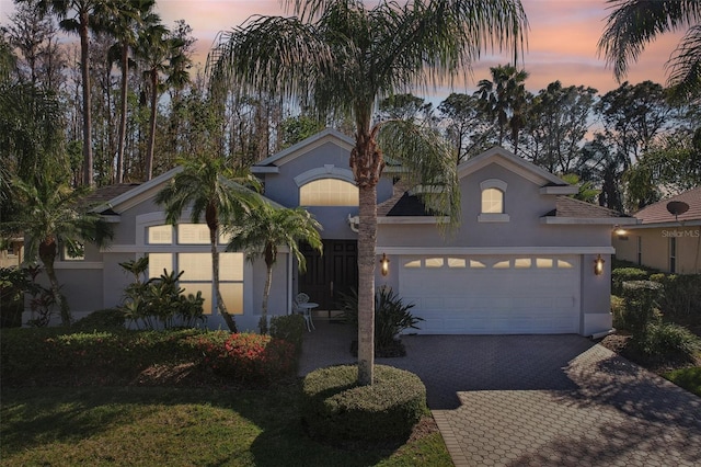 view of front of house with decorative driveway, an attached garage, and stucco siding