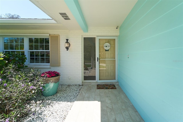 view of exterior entry featuring brick siding and visible vents