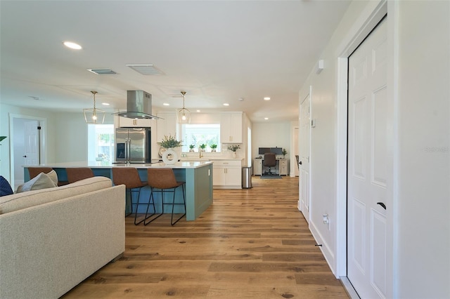 kitchen featuring a breakfast bar, light wood-style floors, white cabinets, island range hood, and stainless steel fridge with ice dispenser