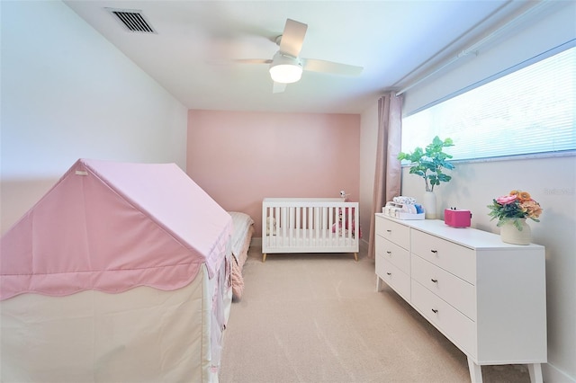 bedroom with light carpet, visible vents, a nursery area, and ceiling fan