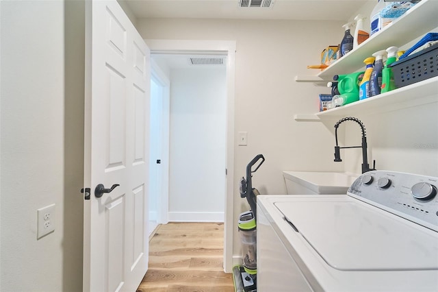 clothes washing area with visible vents, a sink, washer / clothes dryer, light wood finished floors, and laundry area