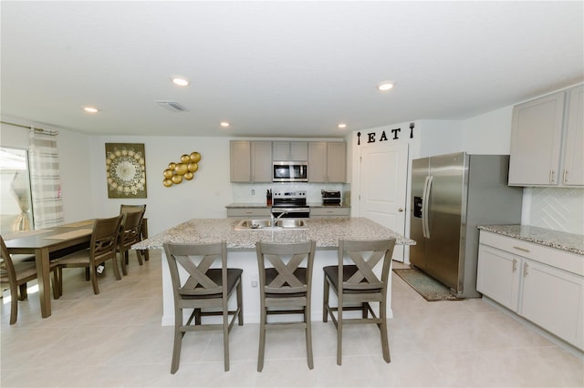 kitchen featuring a center island with sink, visible vents, a sink, appliances with stainless steel finishes, and tasteful backsplash