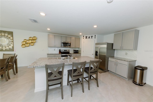 kitchen with visible vents, appliances with stainless steel finishes, a center island with sink, and gray cabinetry