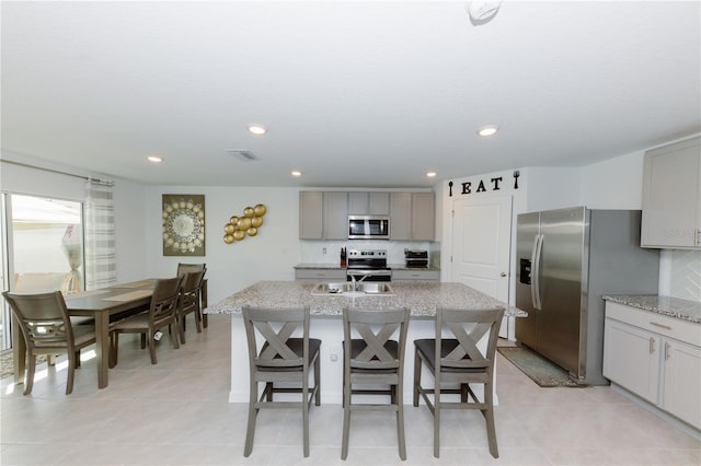 kitchen with a center island with sink, visible vents, gray cabinets, stainless steel appliances, and backsplash