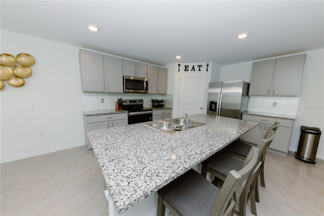 kitchen featuring a sink, a kitchen bar, gray cabinets, appliances with stainless steel finishes, and a kitchen island with sink