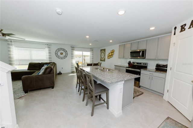 kitchen with gray cabinets, appliances with stainless steel finishes, a breakfast bar, and a kitchen island with sink