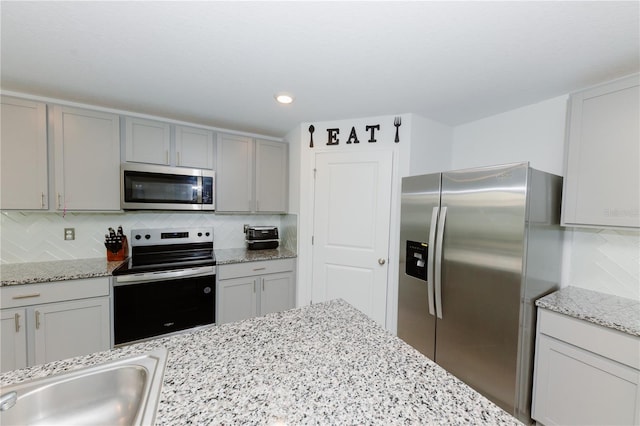 kitchen with gray cabinetry, a sink, appliances with stainless steel finishes, decorative backsplash, and light stone countertops