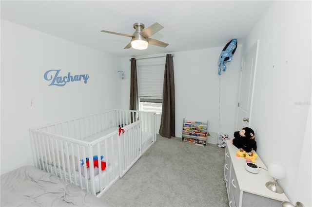 bedroom featuring light colored carpet, a nursery area, and ceiling fan