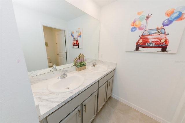 bathroom with double vanity, toilet, baseboards, and a sink