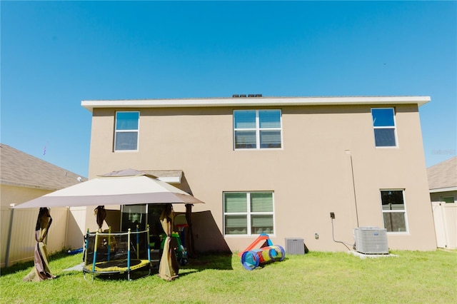 back of house featuring fence, a yard, central AC, stucco siding, and a trampoline