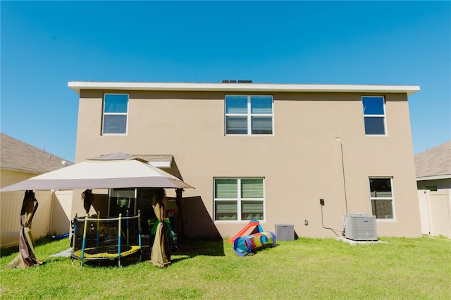 rear view of house featuring fence, a yard, stucco siding, central air condition unit, and a trampoline