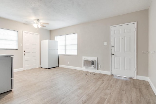 unfurnished living room with a wall mounted air conditioner, light wood-style flooring, a ceiling fan, a textured ceiling, and baseboards