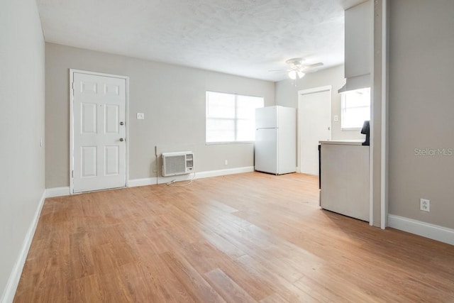 spare room with light wood-style flooring, a ceiling fan, a wall mounted AC, and baseboards