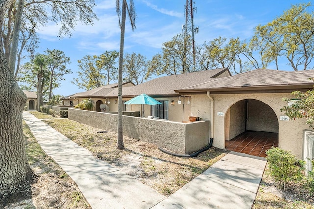 view of side of home featuring stucco siding, roof with shingles, and fence